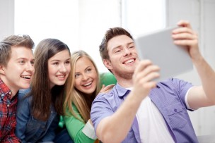education, people, friendship, technology and learning concept - group of happy high school students or classmates with tablet pc computer taking selfie in classroom